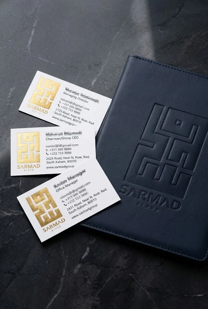 Sarmad Group gold-foil business cards and an embossed navy leather folder on dark marble